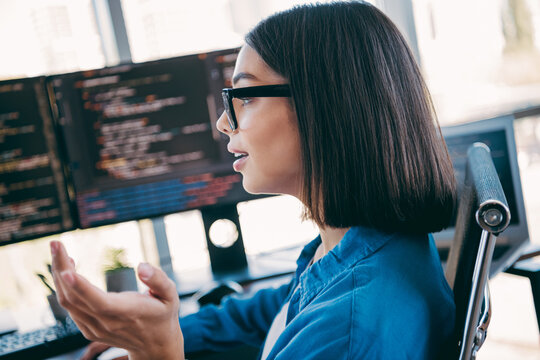 Female programmer working at multiple monitors coding software and discussing a project