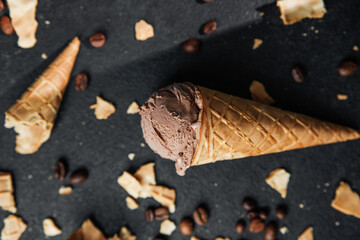 Chocolate ice cream cone with coffee beans and waffle crumbs on dark background