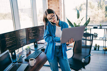 Businesswoman with laptop and multiple monitors in a modern loft office busy with programming and...