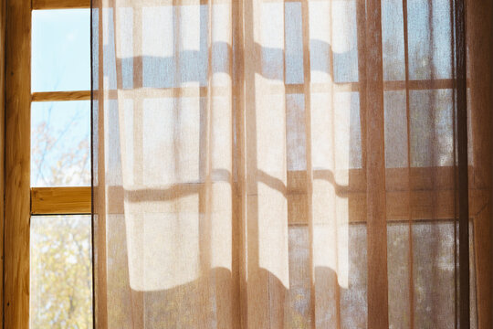 Sunlight through sheer curtain on wooden window frames casting soft geometric shadows indoors