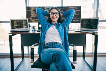 Young female programmer relaxes in a modern loft office with multiple screens showing code and a...