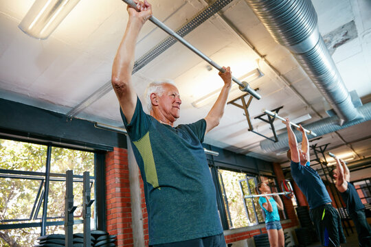 Senior man, barbell and personal trainer in gym for fitness, training and health with body strength class. Bodybuilder, workout and low angle for muscle growth, retirement and exercise with deadlift