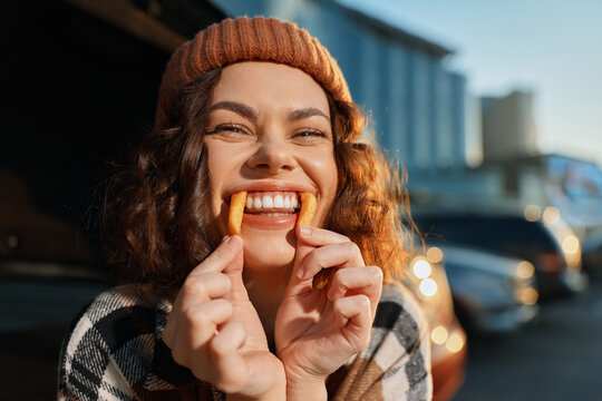 Smiling woman in a beanie holds a snack to her teeth in a playful candid urban portrait with golden hour glow, authenticity and emotional storytelling for mindful living lifestyle. - Powered by Adobe