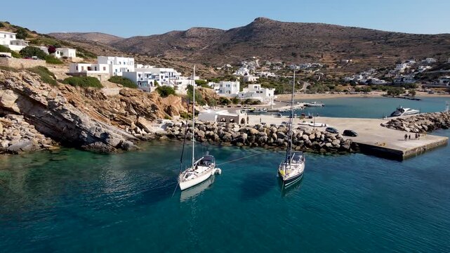 Aerial view of Alopronoia port showcasing boats on turquoise waters near white buildings under a clear sky, Sikinos, Thira, Greece.