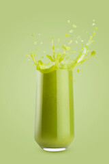 Pulpy green vegetable juice with flying drops, splashing in glass  on green background. Spinach, celery, greens mix smoothie for healthy fitness meny, diet, energy vitamin wholesome cuisine, poster.