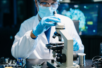IT technician using microscope to inspect a motherboard in a modern lab. Electronics repair,...