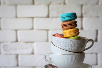 Colorful macarons stacked in white teacups against brick wall