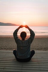 Person meditating at sunrise framing sun with hands