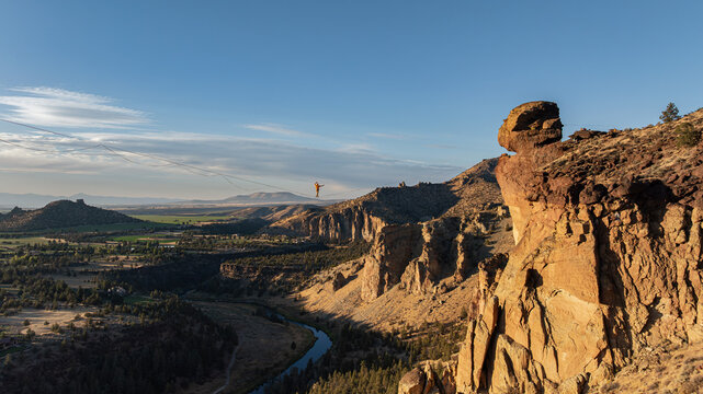 Aerial view of a person on a slackline suspended between rocky cliffs, casting long shadows over the winding river below, Terrebonne, Oregon, United States.