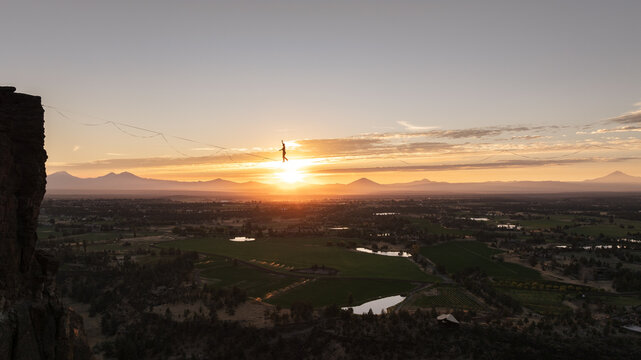 Aerial view of a lone figure poised on a highline silhouetted against the fiery sunset over the vast, patterned landscape of Terrebonne, Oregon, United States.
