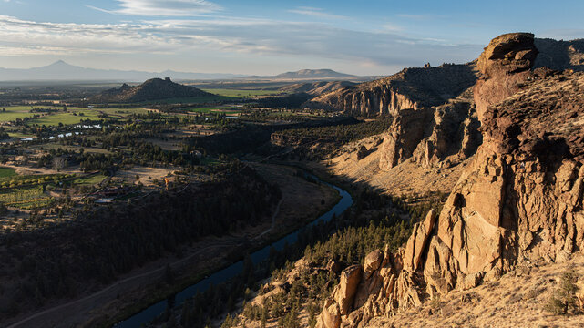 Aerial view of the winding Crooked River carving through rugged canyons and fertile valleys, contrasting sunlit cliffs with shadowy depths, Terrebonne, Oregon, United States.