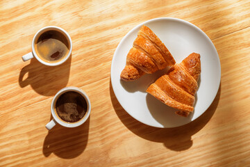 Two espresso cups and croissant in morning sun rays
