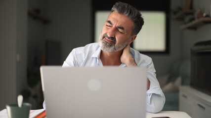 Man feeling neck pain working on laptop