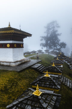 Aerial view of white stupas with golden roofs stand in misty air against the backdrop of green hills, Druk Wangyal Chortens, Dochula Pass, Bhutan.