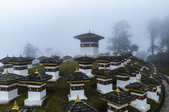 Aerial view of the Druk Wangyal Chortens shrouded in mist, where white stupas with golden roofs punctuate the landscape, Dochula Pass, Bhutan.