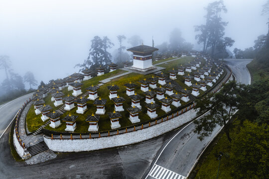 Aerial view of the Druk Wangyal Chortens rising through the mist-veiled landscape, a tapestry of white stupas and verdant foliage, Dochula Pass, Bhutan.