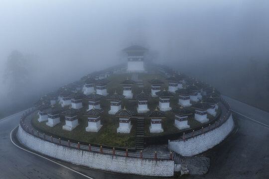 Aerial view of the Druk Wangyal Chortens shrouded in a thick veil of mist, creating an ethereal ambiance, Dochula Pass, Bhutan.