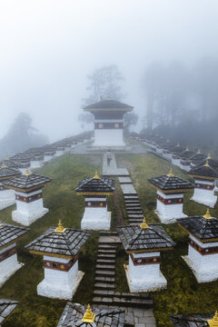 Aerial view of the Druk Wangyal Chortens emerges from the misty heights, a serene tapestry of white and gold against the muted green landscape, Dochula Pass, Bhutan.
