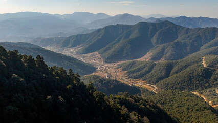 Aerial view of sun-kissed peaks embracing a valley town, nestled between lush green hills and winding roads, Chandragiri, Bagmati Province, Nepal.