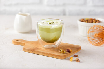Pistachio matcha latte with coconut cream in a glass with bamboo chasen on a wooden board.