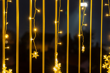 Close-up of small warm LED lights and snowflake ornaments hanging on a balcony, producing starburst effects in the dark