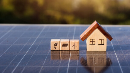 Wooden house model with renewable energy icons on solar panel surface.