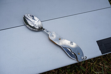 A foldable metal dining spoon for outdoor and camping activities placed on a portable folding table.