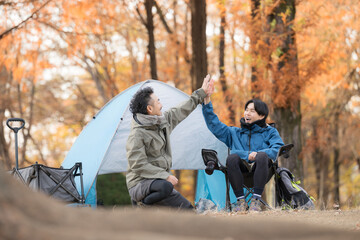 Two men smiling in front of their tent at an autumn campground, striking a pose for an outdoor holiday scene. High-fiving in joy.