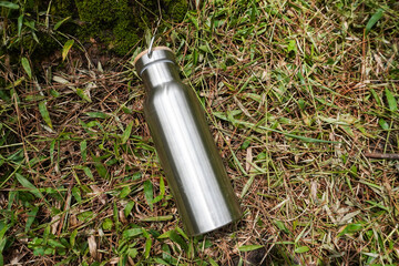 A silver stainless steel tumbler placed on a grassy surface. Flatlay high top angle view.	