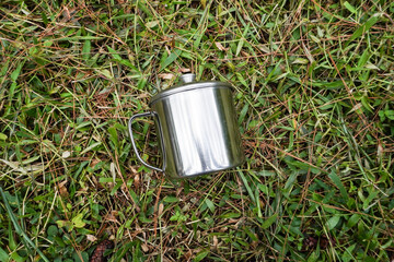 A silver-colored stainless steel mug placed on a grassy surface. Flatlay high top angle view.	