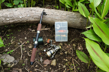 A fishing rod with a fishing reel, tackle box, fishing line spool placed on a rocky surface during fishing activities.