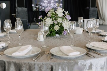 Elegant wedding table setting with grey tablecloth, white plates, crystal glasses and floral centerpiece of white roses