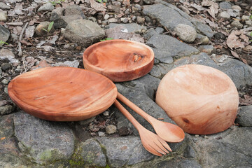 Empty wooden plates, bowls, and spoons and forks placed on a rocky surface.
