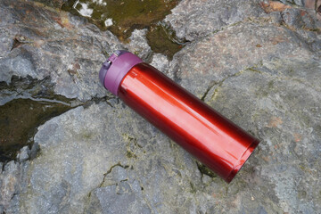 A red insulated tumbler placed on a stone surface.