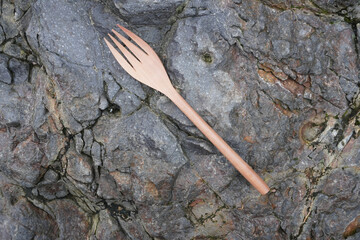 A wooden fork placed on a rough stone surface. Flatlay high top angle view.