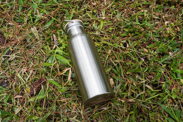 A silver stainless steel tumbler placed on a grassy surface. Flatlay high top angle view.