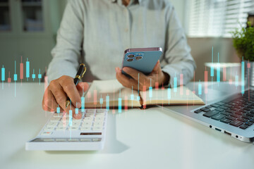 Business woman working on desk office with using a calculator to calculate the numbers and business report talk smart phone on office desk, finance accounting concept.