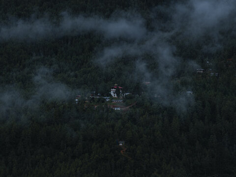 Aerial view of a Dzong nestled amidst a sea of deep green forests, veiled in ethereal mist, standing as a beacon of serenity, Paro, Bhutan.