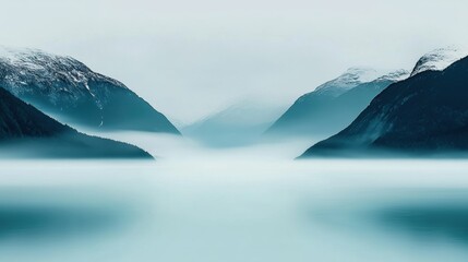 A serene landscape of snow-capped mountains, a calm lake, and a hazy sky.