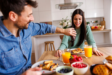Couple putting chocolate topping on waffles while having breakfast at home