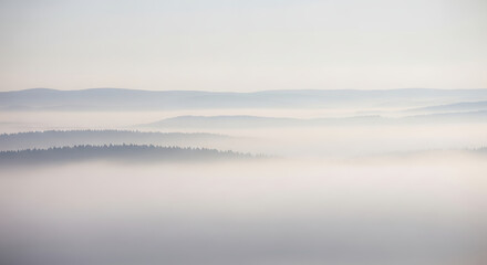 Fototapeta premium Foggy Mountain Landscape Featuring Layers of Forested Ridges Obscured by Mist Creating Serene and Ethereal Natural Background in Soft Light
