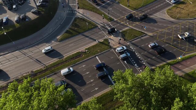 Aerial drone shot showing traffic at a large urban intersection with cars, motorcycles, road markings, and pedestrian lanes during daytime.