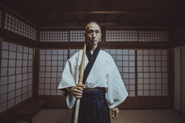 Senior kendo sensei practicing an ancient japanese martial art, doing a training exercise with a shinai in a traditional dojo with shoji screens and tatami mats