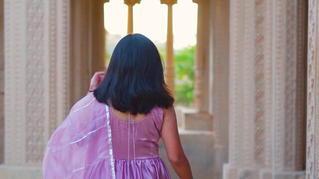 Rear view of Indian woman inside sacred ancient Indian temple at Kutch, Gujarat, India. Woman in a salwar suite walking through Hindu temple with carved stone pillars, arches and windows. 