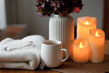 Cozy winter home interior with warm candlelight, wool sweater, hot tea and LED decor creating a calm hygge atmosphere