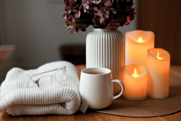 Cozy winter home interior with warm candlelight, wool sweater, hot tea and LED decor creating a calm hygge atmosphere