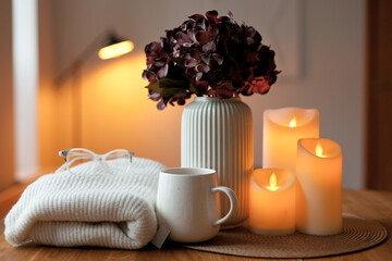 Cozy winter home interior with warm candlelight, wool sweater, hot tea and LED decor creating a calm hygge atmosphere