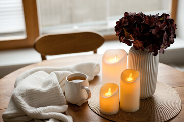 Cozy winter home interior with warm candlelight, wool sweater, hot tea and LED decor creating a calm hygge atmosphere