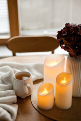 Cozy winter home interior with warm candlelight, wool sweater, hot tea and LED decor creating a calm hygge atmosphere