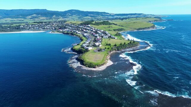 Drone aerial landscape of Gerroa headland and rugged rocky coastline with ocean reef waves and residential rural town homes along main road street on the South Coast Australia travel vacation tourism